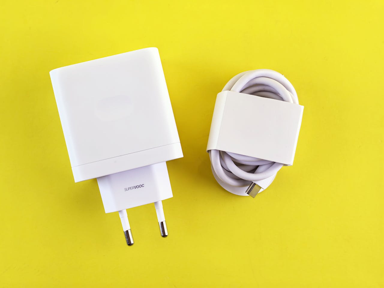 White SuperVOOC charger and cable on a bright yellow background, showcasing minimalist design.