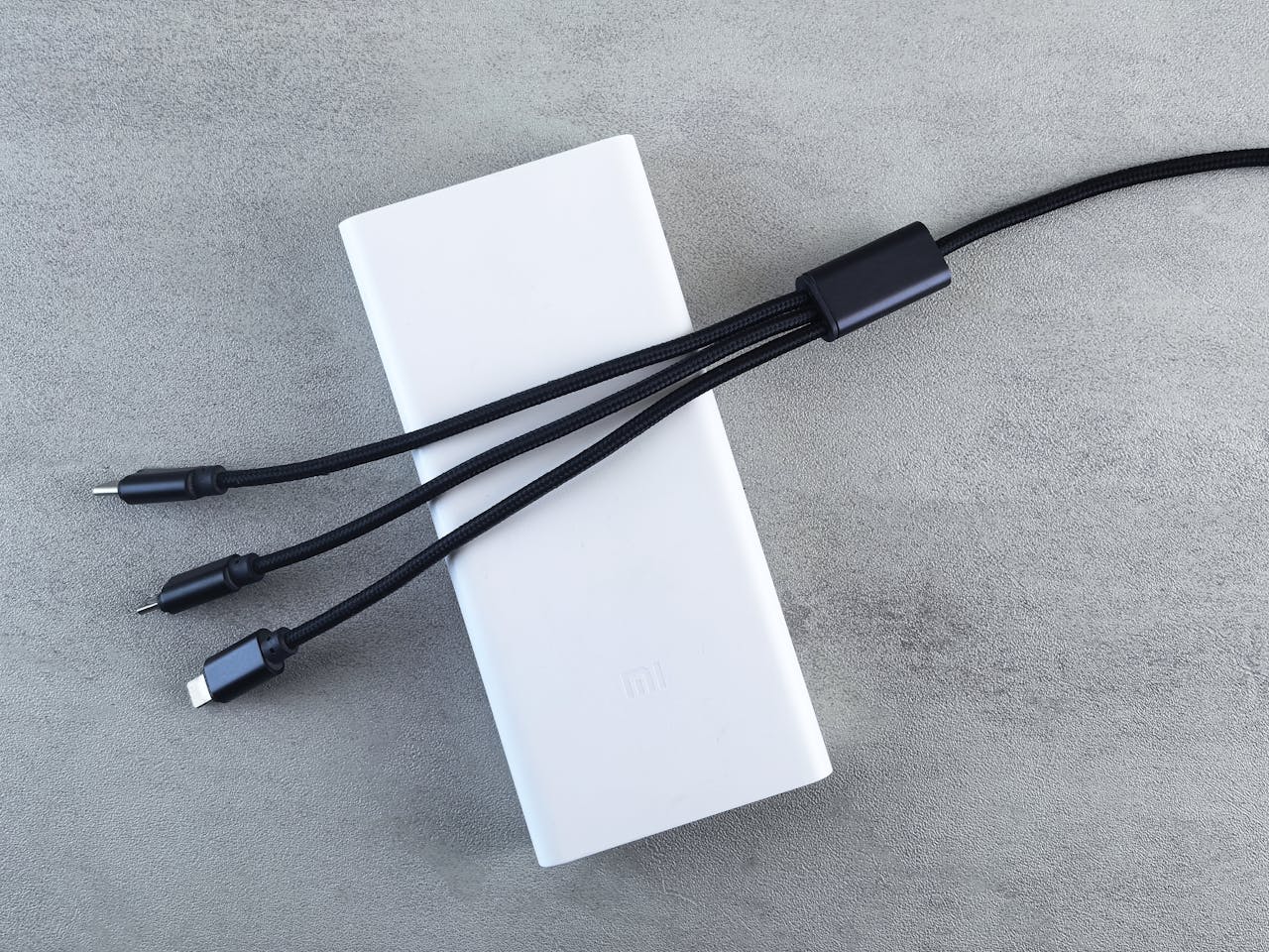 A sleek white power bank with a black multi-connector cable laid on a textured grey surface, emphasizing modern technology.